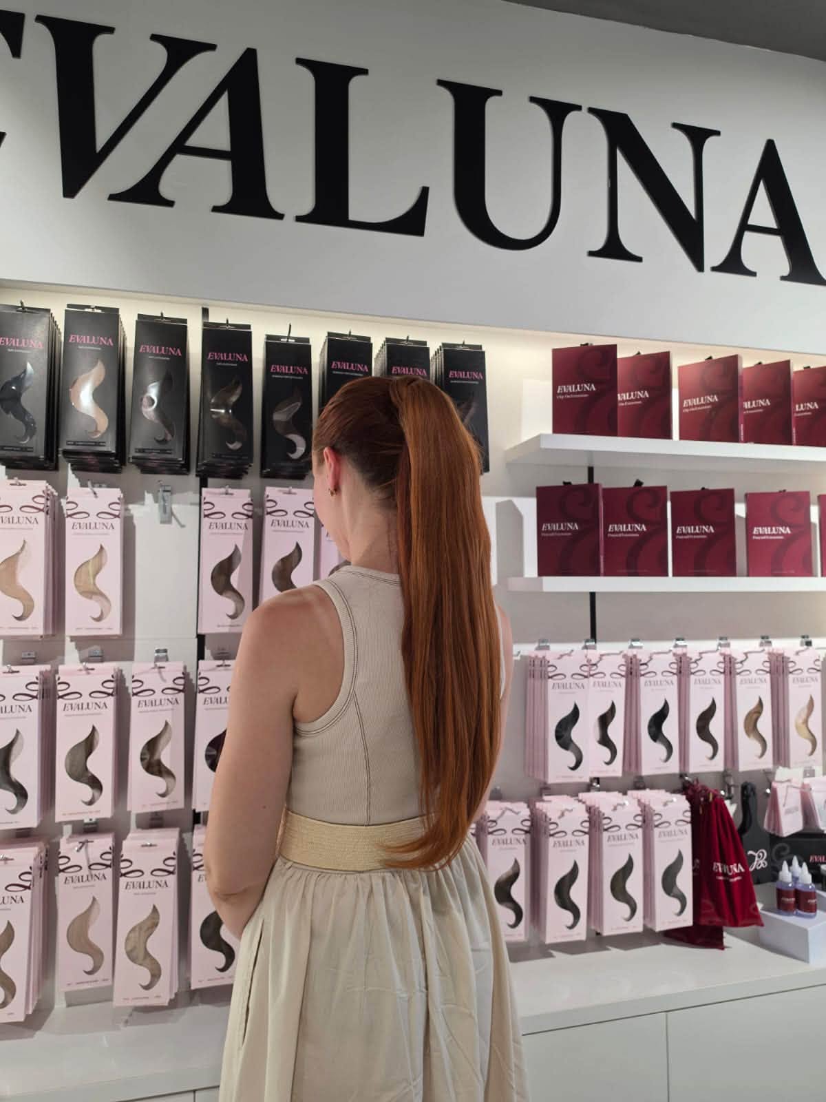 Client browsing the EvaLuna boutique display wall of packaged hair extensions in Malta